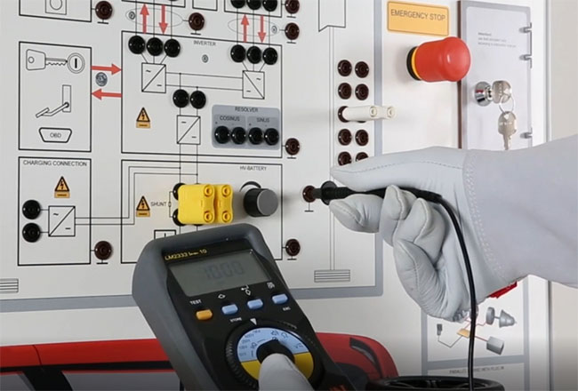 Hands-on electric vehicle diagnostics training with high-voltage safety equipment Technician measuring voltage on an electric vehicle training panel using a digital multimeter and insulated gloves