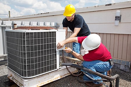 Two repairmen working on an HVAC system repair